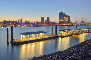 Deutschland, Hamburg, Nördliches Elbufer in der Morgendämmerung mit Elbphilharmonie und Stadtsilhouette im Hintergrund - RJF00839