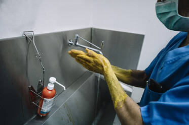 Male doctor scrubbing hands by sink at hospital - JCMF01688