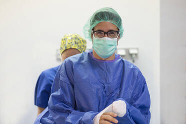 Männlicher Chirurg mit Brille und Mitarbeiterin im Krankenhaus - JCMF01690