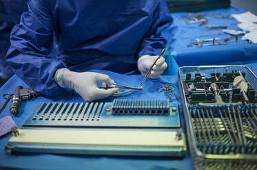 Männlicher orthopädischer Chirurg bereitet eine Pinzette für eine Operation auf der Intensivstation vor - JCMF01693