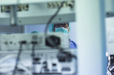 Focused male surgeon looking at monitoring equipment while operating in ICU - JCMF01697