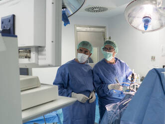 Male doctors watching monitoring equipment while operating patient at hospital - JCMF01714