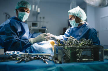 Männlicher Chirurg geht an medizinischer Ausrüstung vorbei, während er eine Operation im Operationssaal durchführt - JCMF01720