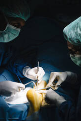 Männliche Chirurgen bei einer Operation am Knöchel in einer dunklen Notaufnahme - JCMF01721