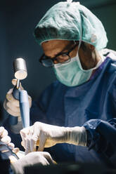 Male surgeon using hammer while doing ankle surgery in operating room - JCMF01724