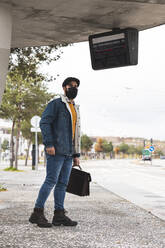 Pendler mit Hut beim Warten auf den Bus während COVID-19 - JAQF00025