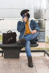 Commuter on phone call looking away while sitting at bus stop during COVID-19 - JAQF00040