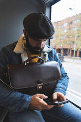 Commuter with briefcase using smart phone by window in bus - JAQF00045