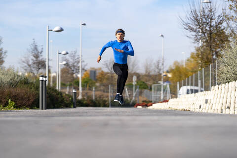 Sportler läuft mit Hingabe auf dem Fußweg in einem öffentlichen Park an einem sonnigen Tag, lizenzfreies Stockfoto