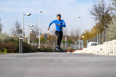 Sportsman running with dedication on footpath in public park on sunny day - GGGF00507