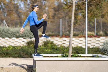 Junge männliche Sportlerin, die an einer Stützmauer in einem öffentlichen Park an einem sonnigen Tag trainiert - GGGF00510