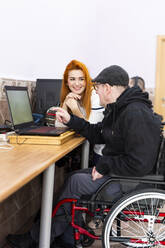 Smiling female caregiver talking with disabled man by laptop at nursing home - LJF01929