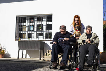 Behinderte Frau und Mann mit Pflegerin, die einen Hund vor einem Rehabilitationszentrum halten - LJF01993