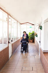 Weibliche Krankenschwester hilft behindertem Mann im Rollstuhl sitzend auf dem Flur eines Pflegeheims - LJF02010