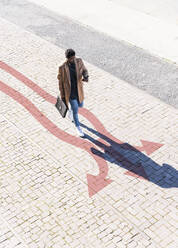Well-dressed man walking along arrows stretching across sidewalk - UUF22292