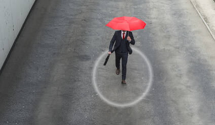 Businessman walking along street with red umbrella in hand - UUF22295