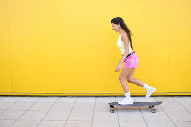 Beautiful girl skateboarding along yellow wall in summer - AODF00067