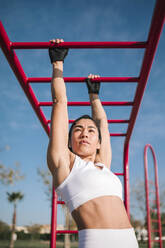 Female athlete exercising on monkey bars in public park on sunny day - GRCF00556