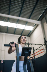 Lächelnde Sportlerin bei der Arbeit an einem Trainingsgerät im Fitnessstudio - GRCF00565