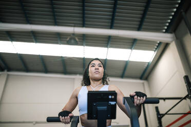 Selbstbewusste Sportlerin an einem Trainingsgerät im Fitnessstudio - GRCF00566