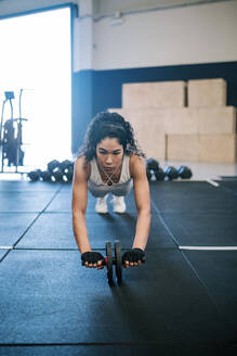 Weibliche Athletin beim Training mit einem Bauchtrainingsrad im Fitnessstudio - GRCF00572