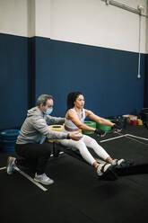 Männlicher Fitnesstrainer trainiert eine Sportlerin im Fitnessstudio während COVID-19 - GRCF00575
