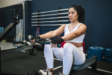 Selbstbewusste Sportlerin, die beim Training im Fitnessstudio am Rudergerät zieht - GRCF00576