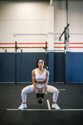 Sportswoman with dedication lifting up kettlebell in gym - GRCF00577