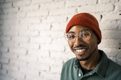 Smiling man wearing eyeglasses against white brick wall - RCPF00497