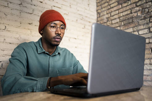 Geschäftsmann, der an einem Laptop an einer Backsteinmauer am Tisch arbeitet - RCPF00519