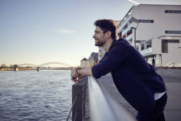 Smiling businessman looking away while leaning on railing - RHF02564