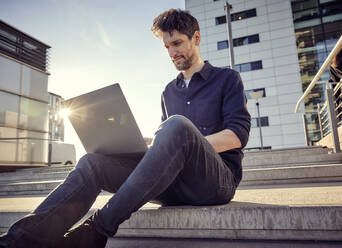 Businessman working on laptop while sitting on steps - RHF02574