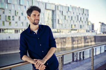 Smiling businessman looking away while leaning on railing - RHF02578