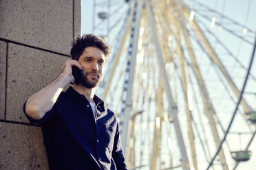 Businessman talking on mobile phone while standing against ferris wheel - RHF02583