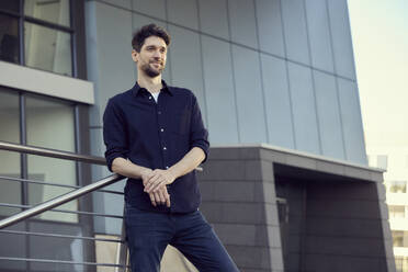 Confident businessman smiling while leaning on railing - RHF02590