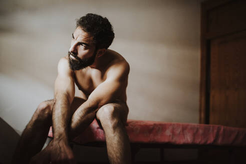 Thoughtful naked man looking away while sitting on bed - MIMFF00333