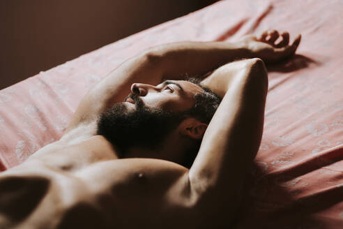 Young shirtless man resting in bedroom at home - MIMFF00339