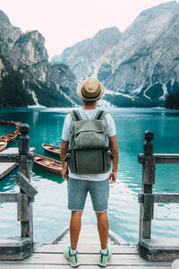 Rückenansicht eines nicht erkennbaren männlichen Reisenden, der auf einem hölzernen Kai steht und die herrliche Szenerie eines Sees mit türkisfarbenem Wasser in den Bergen an einem nebligen Tag bewundert - ADSF19364