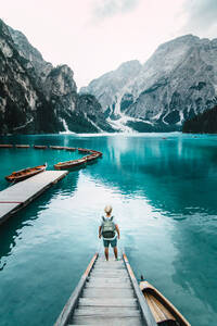 Back view of unrecognizable male traveler standing on wooden quay and admiring amazing scenery of lake with turquoise water in mountains on foggy day - ADSF19365