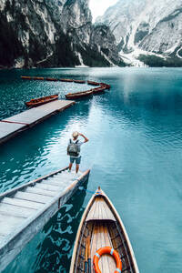 Rückenansicht eines nicht erkennbaren männlichen Reisenden, der auf einem hölzernen Kai steht und die herrliche Szenerie eines Sees mit türkisfarbenem Wasser in den Bergen an einem nebligen Tag bewundert - ADSF19367