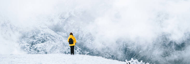 Back view of anonymous hiker with trekking poles walking on snowy ground in Pyrenees mountains in Andorra - ADSF19369