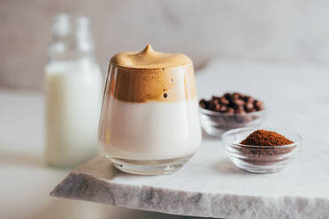 Aromatisches Dalgona-Getränk im Glas auf einem Marmortisch mit Instantkaffee und Bohnen - ADSF19373