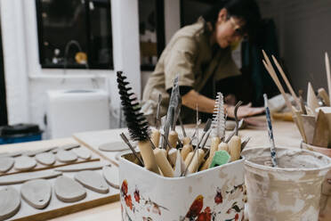 Craftsman shaping piece of clay with wooden rolling pin while creating handicraft earthenware in art workshop - ADSF19384