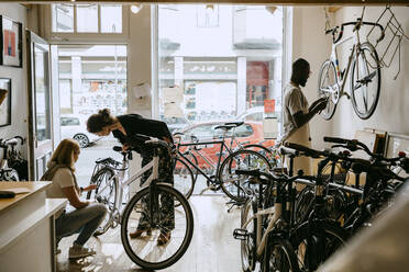 Female owner repairing bicycle of senior customer while colleague working on bike at workshop - MASF21029