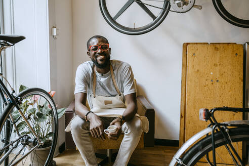 Porträt eines männlichen Besitzers mit Kaffeetasse in einem Fahrradgeschäft - MASF21065