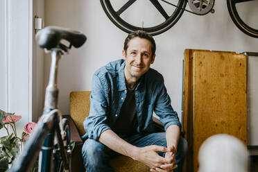 Portrait of smiling male owner sitting in bicycle shop - MASF21070
