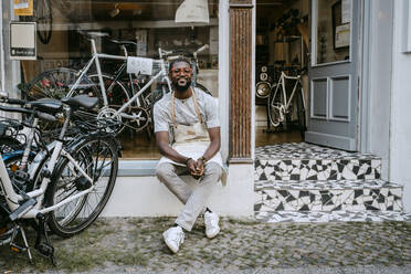 Portrait of male owner sitting against bicycle shop - MASF21072