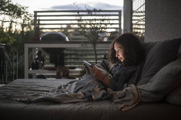 Seitenansicht eines Teenagers, der ein digitales Tablet benutzt, während er sich auf dem Sofa zu Hause entspannt - MASF21082