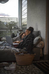 Mother and daughter watching laptop while resting on sofa at home - MASF21085