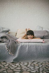 Porträt eines lächelnden Mädchens, das zu Hause auf dem Sofa liegt - MASF21093